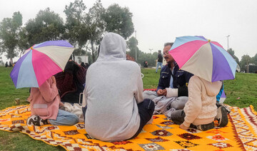 People sit with umbrellas along a promontory in al-Namas in Saudi Arabia's Asir province, on August 16, 2022. (AFP)